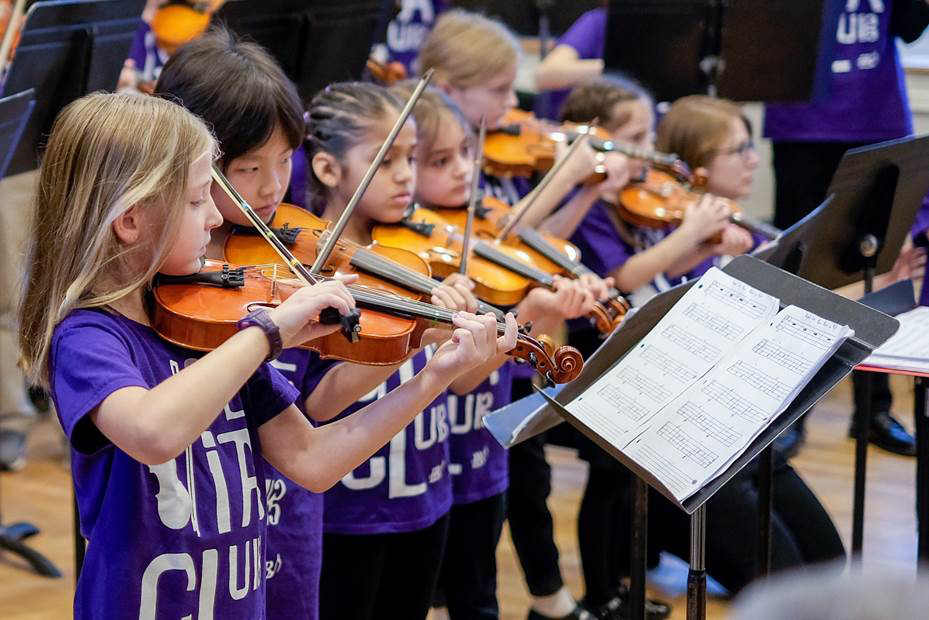 Young girls in purple t shirts playing the viola.